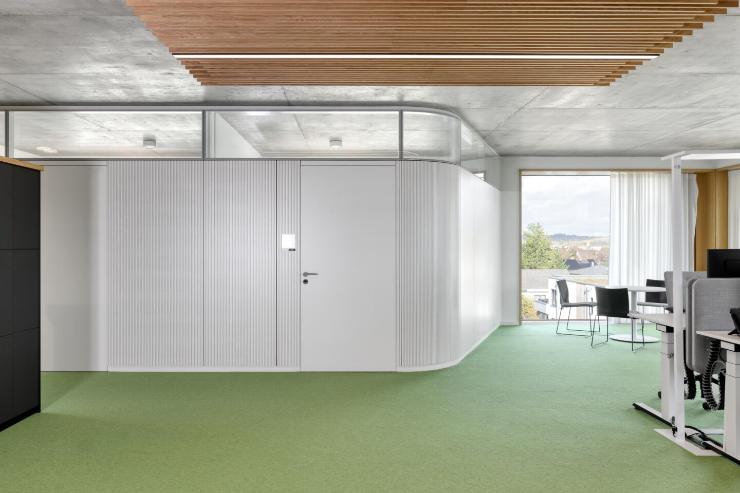 Gerundete Systemtrennwand aus Glas in Kombination mit einer flächenbündigen Holztür für moderne Büros.