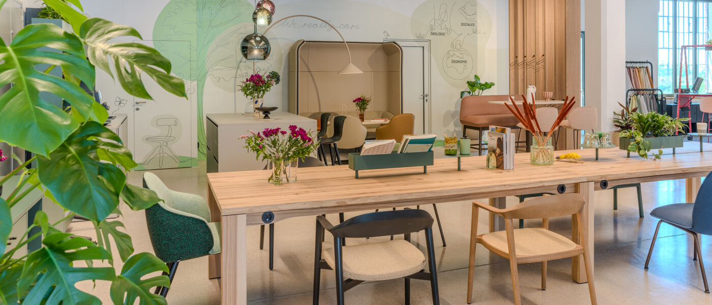 Großer Echtholz-Konferenztisch mit Monstera-Pflanzen im Vordergrund und Holz-Akustikwand im Showroom