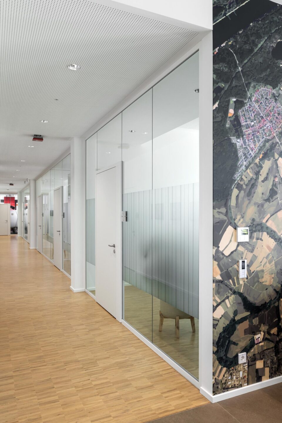 Lichtdurchfluteter Flur der Sparkasse Rheinstetten mit fecoplan Flurglaswand, weißer Holztür und regionaler Wandgrafik