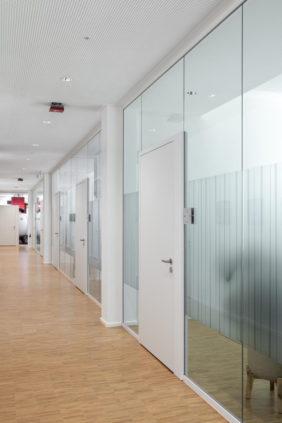 Zargenbündige weiße Holztür integriert in eine fecoplan Glaswand mit Sichtschutzfolierung im Flur der Sparkasse
