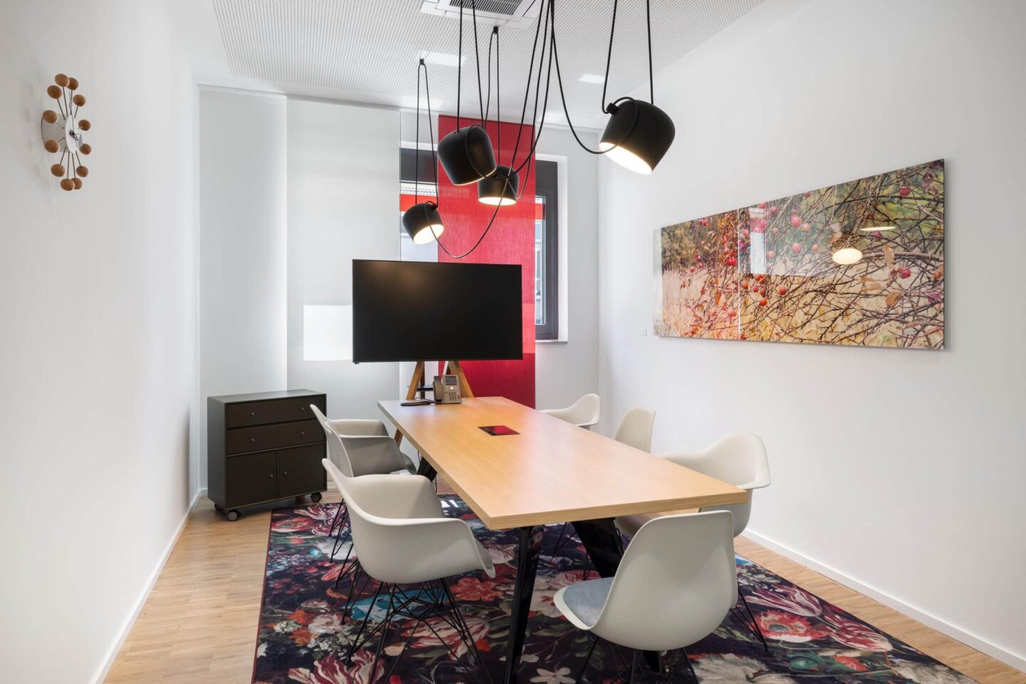 Besprechungsraum mit Holz-Konferenztisch, Vitra-Stühlen, Blumenmotive-Teppich und schwarzer Designer-Pendelleuchte