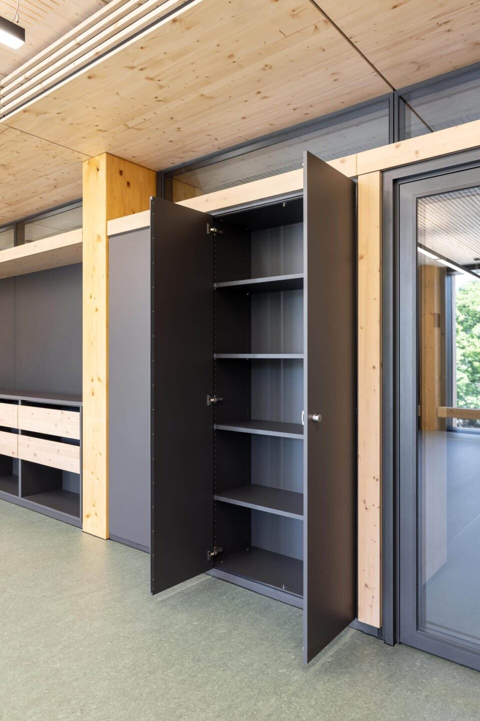 Opened feco cabinet wall with shelves next to a glazed aluminum frame door in the new wooden building of Zollberg-Realschule.